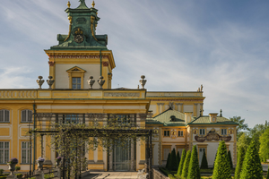 Zabytkowy pałac otoczony kolorowymi żywopłotami i kwiatami, na tle nieba.