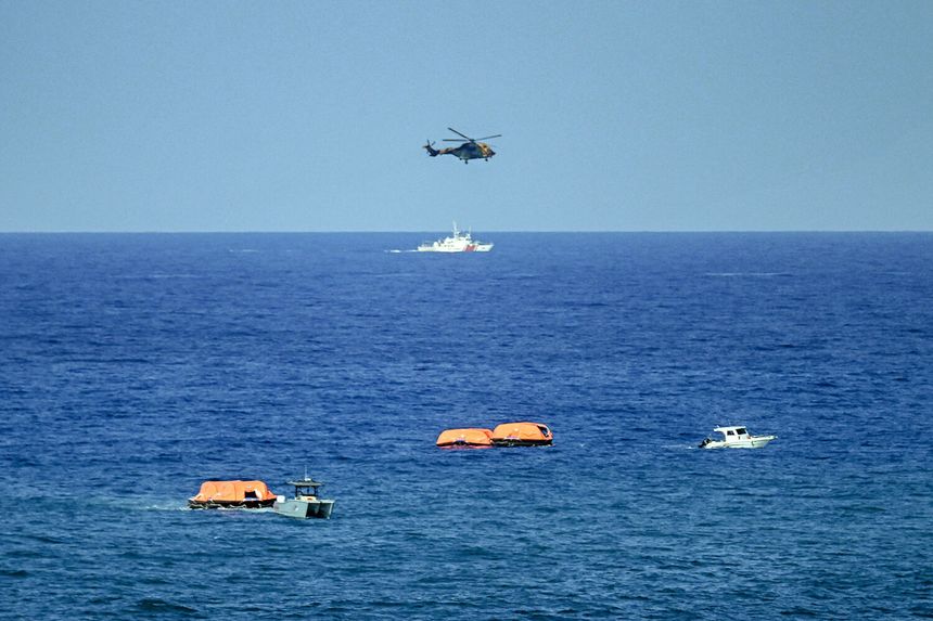 Na zdjęciu widoczny helikopter nad wodą oraz łodzie z pomarańczowymi tratwami ratunkowymi.
