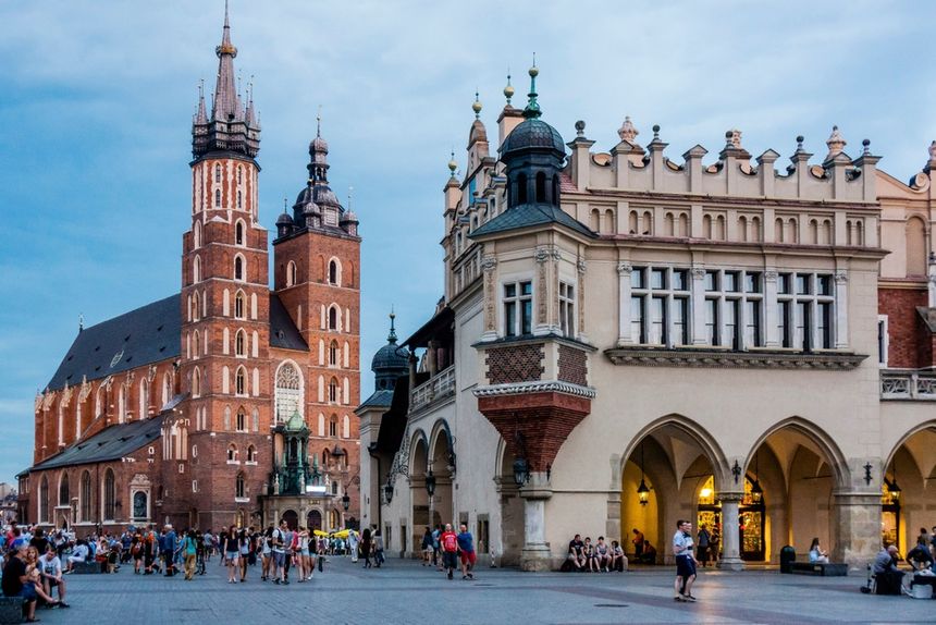 Na zdjęciu widać Sukiennice i Kościół Mariacki w Krakowie. Wieczorna sceneria z ludźmi.