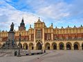 Widok na Sukiennice w Krakowie z pomnikiem w centrum oraz niebem w tle.