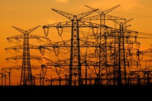 Silhouette wysokich słupów energetycznych na tle zachodzącego słońca.