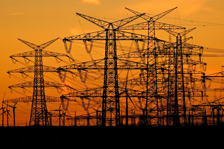 Silhouette wysokich słupów energetycznych na tle zachodzącego słońca.