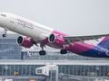 Samolot linii Wizz Air startujący z lotniska, w tle budynki terminalu. Szare niebo.