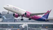 Samolot linii Wizz Air startujący z lotniska, w tle budynki terminalu. Szare niebo.