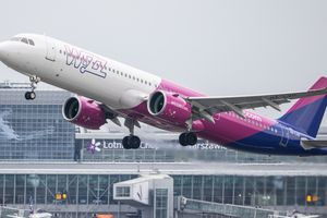 Samolot linii Wizz Air startujący z lotniska, w tle budynki terminalu. Szare niebo.