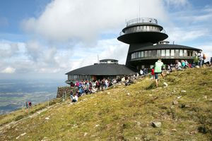 Widok na budynek górski z grupą ludzi na zielonej strefie i chmurami na niebie.