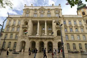 Historyczny budynek z kolumnami, nad nim niebo z chmurami, uliczni przechodnie.