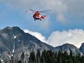 Helikopter ratunkowy przelatuje nad górskim krajobrazem, z masywnymi szczytami w tle.