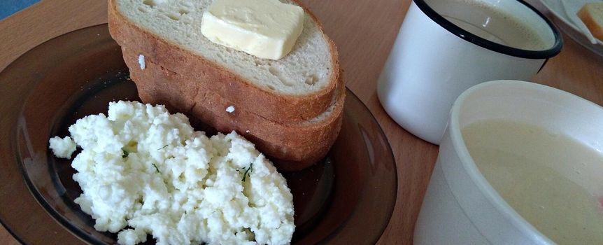 Talerz z kromką chleba z masłem, serem białym i filiżanką kawy na drewnianym stole.