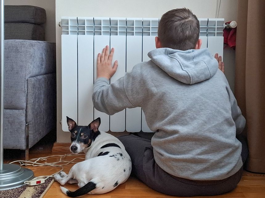 chłopiec ogrzewa się przy ciepłym kaloryferze