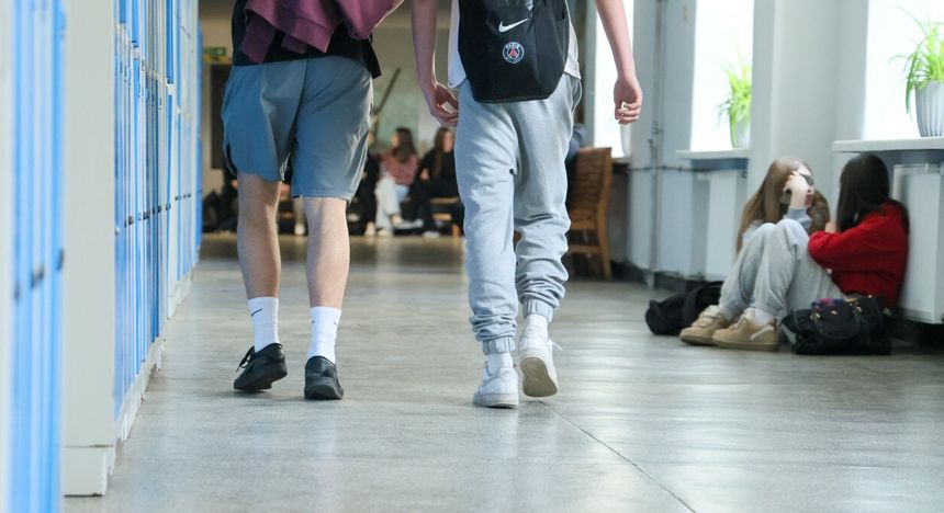 Dwa młode osoby w dresach idą korytarzem, w tle grupy uczniów siedzących w szkole.