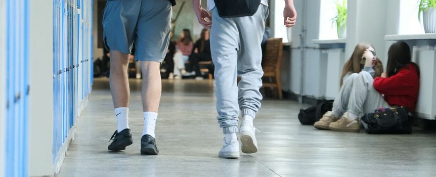 Dwa młode osoby w dresach idą korytarzem, w tle grupy uczniów siedzących w szkole.