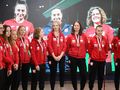 reprezentacja Polski w amp futbolu kobiet w czerwonych strojach, z medalami, przed tłem z ich zdjęciem.