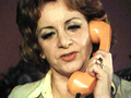 Kobieta z kręconymi włosami rozmawia przez telefon w kolorze pomarańczowym.