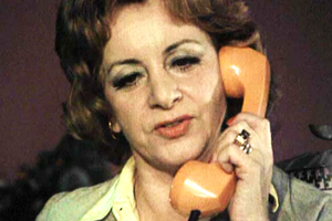 Kobieta z kręconymi włosami rozmawia przez telefon w kolorze pomarańczowym.
