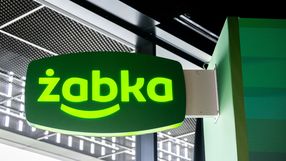 Zielony znak ze stylizowanym napisem „żabka” w sklepie convenience.