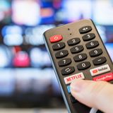 Pilot z przyciskami do TV, trzymany w dłoni, w tle rozmyty ekran telewizora.