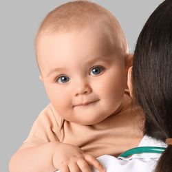 Na zdjęciu uśmiechnięte niemowlę trzymane przez osobę w białym fartuchu lekarskim.
