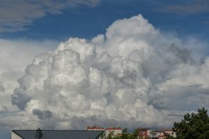 Chmury w jasnym kolorze otaczają niebo, z fragmentem budynków w dolnej części kadru.