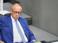 Mężczyzna w niebieskim garniturze siedzi na sali obrad. Obok leży telefon.
