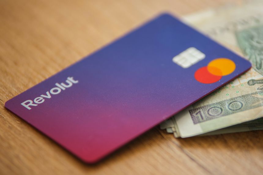 Karta Revolut leży na stole obok banknotów. Kolory karty: fioletowy, czerwony, żółty.