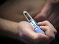 Mężczyzna trzyma ręczny aplikator leku na brzuchu, przygotowując się do wstrzyknięcia.