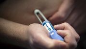 Mężczyzna trzyma ręczny aplikator leku na brzuchu, przygotowując się do wstrzyknięcia.