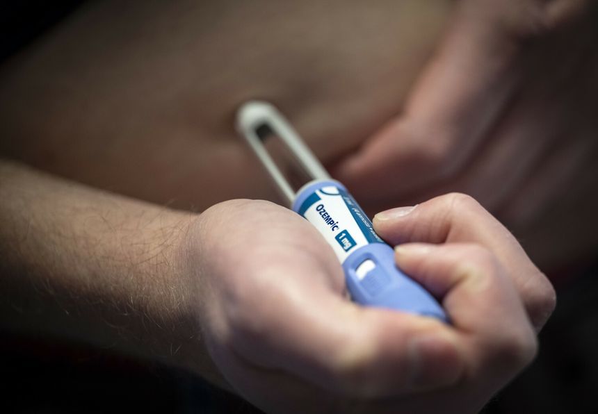 Mężczyzna trzyma ręczny aplikator leku na brzuchu, przygotowując się do wstrzyknięcia.