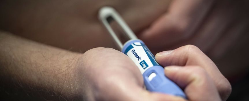 Mężczyzna trzyma ręczny aplikator leku na brzuchu, przygotowując się do wstrzyknięcia.