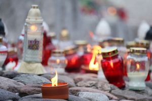 Stos żarówek w różnych kolorach, wśród nich świeca w doniczce na kamieniach.