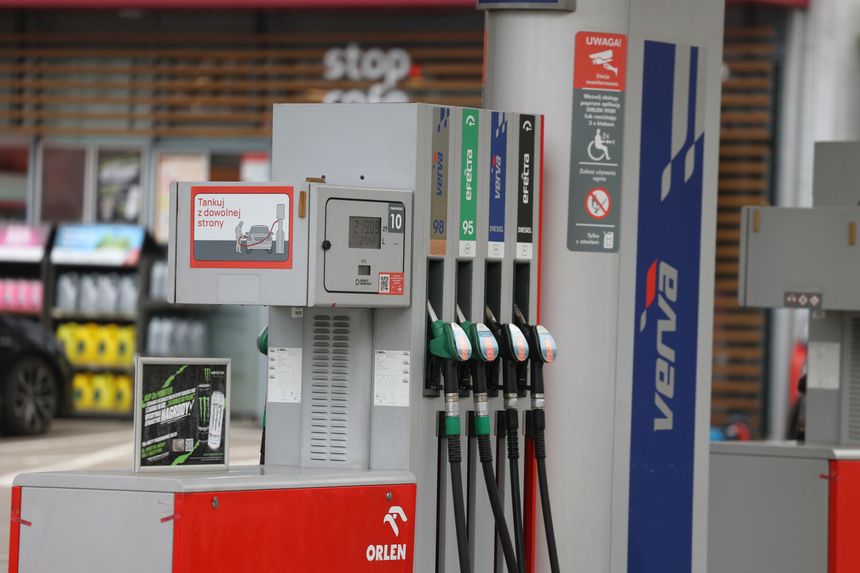 Stacja paliw z dystrybutorami. W tle reklama napoju energetycznego i informacja o tankowaniu.