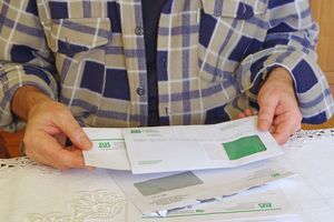 Mężczyzna trzyma listy ZUS, siedząc przy stole nakrytym serwetką. Ubrany w koszulę w kratę.