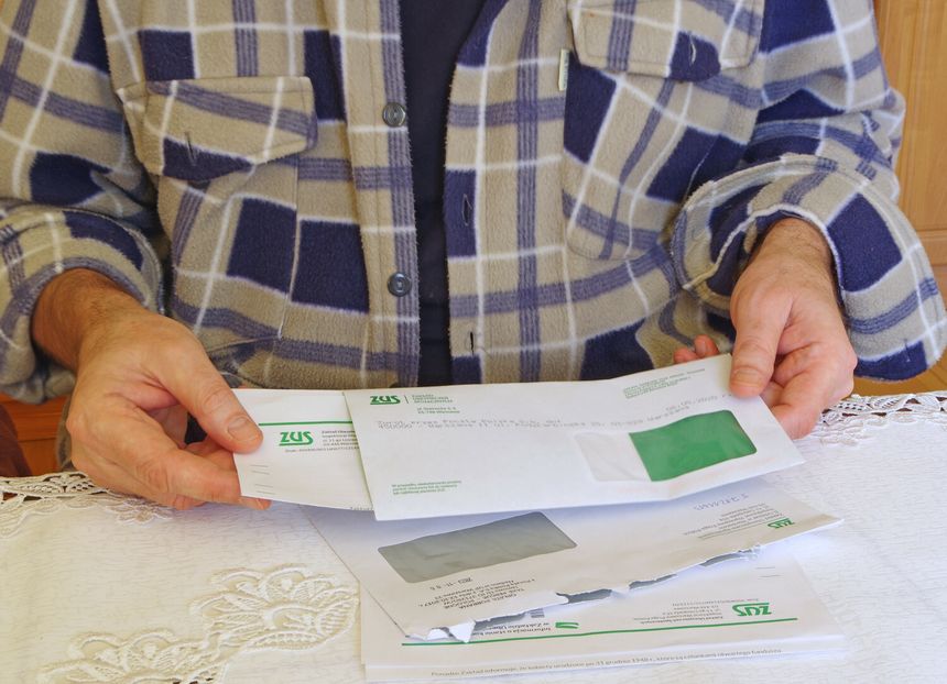 Mężczyzna trzyma listy ZUS, siedząc przy stole nakrytym serwetką. Ubrany w koszulę w kratę.