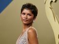 Zendaya o krótkich włosach, w eleganckiej sukni, z biżuterią, patrzy w stronę obiektywu.