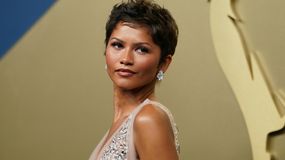 Zendaya o krótkich włosach, w eleganckiej sukni, z biżuterią, patrzy w stronę obiektywu.