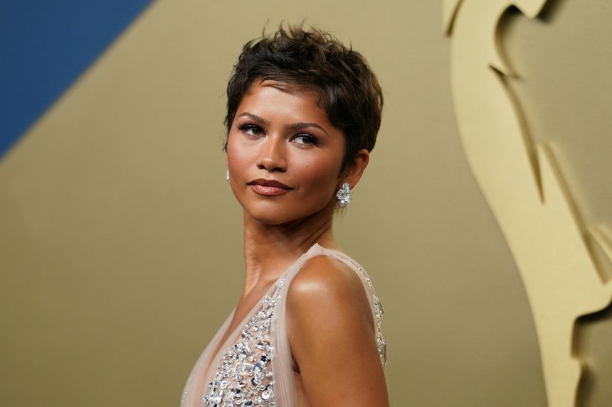 Zendaya o krótkich włosach, w eleganckiej sukni, z biżuterią, patrzy w stronę obiektywu.