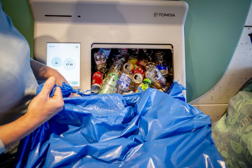 Osoba z niebieską torbą zbiera surowce do recyklingu przy automacie. Wyświetlacz pokazuje ilość i wartość.