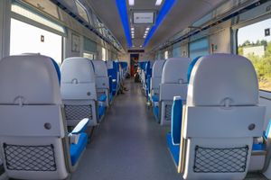 Wnętrze nowoczesnego pociągu, rzędy niebieskich siedzeń, duże okna po obu stronach.