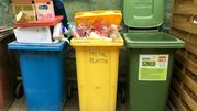 Na zdjęciu trzy pojemniki na odpady: niebieski na papier, żółty na metale i plastik, zielony na szkło.
