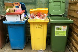 Na zdjęciu trzy pojemniki na odpady: niebieski na papier, żółty na metale i plastik, zielony na szkło.