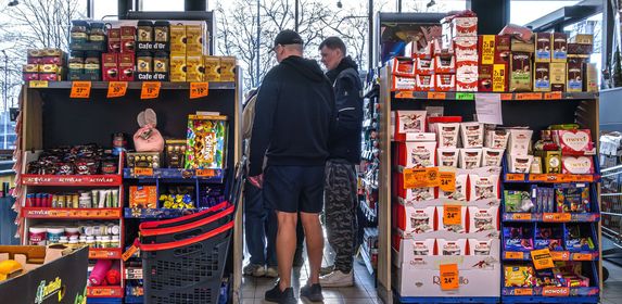 Grupa mężczyzn w supermarkecie, przeszukująca regały z produktami spożywczymi.