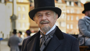 Mężczyzna w kapeluszu cylindrycznym i eleganckim płaszczu, uśmiechający się na tle miasta.
