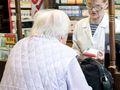 Na zdjęciu starsza kobieta rozmawia z farmaceutką w aptece, obie w jasnych ubraniach.