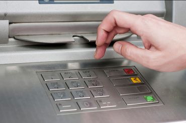 Ręka nad klawiaturą bankomatu, gotowa do nacisnięcia klawisza. Metalowa obudowa urządzenia.