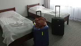 Dwa łóżka w pokoju hotelowym, obok bagaże: niebieska walizka, czarna walizka i brązowa torba.