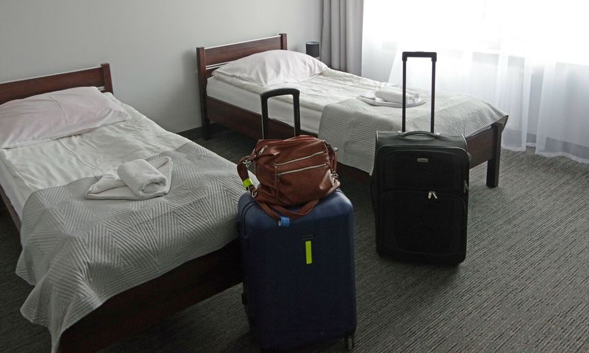 Dwa łóżka w pokoju hotelowym, obok bagaże: niebieska walizka, czarna walizka i brązowa torba.