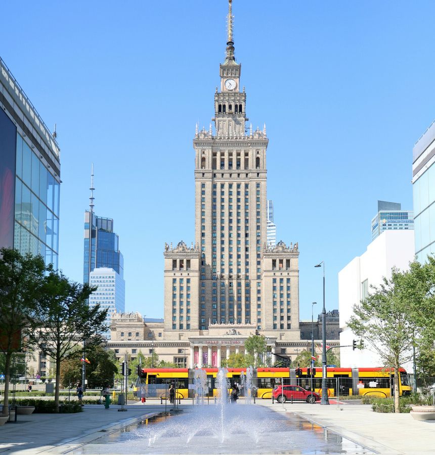 Warszawski Pałac Kultury i Nauki w słoneczny dzień, w tle miasto i fontanna.