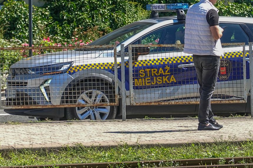 Na zdjęciu widoczny jest samochód straży miejskiej oraz stojący mężczyzna.