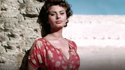 Sophia Loren. Na zdjęciu kobieta o ciemnych włosach w koronkowej bluzce, stojąca przy kamiennej ścianie.