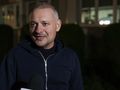 Mężczyzna w ciemnym ubraniu uśmiecha się, stojąc przed budynkiem w nocy.